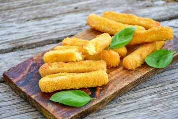 Vegetarian cheese breaded  oven baked  mozzarella sticks with  fresh basil on wooden background 