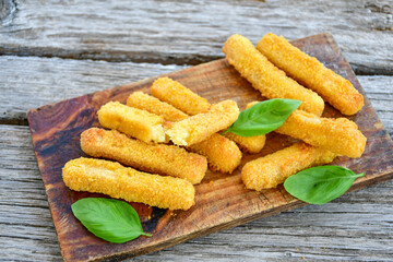 Vegetarian cheese breaded  oven baked  mozzarella sticks with  fresh basil on wooden background 