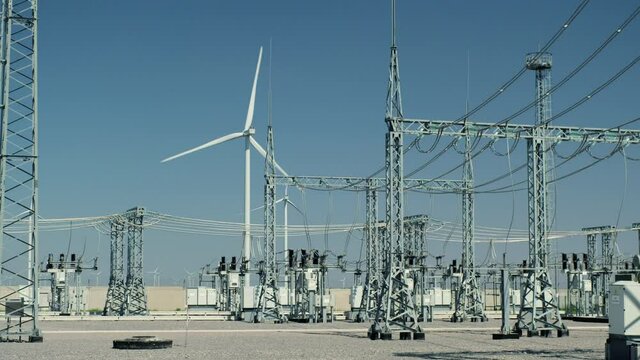 Wind turbine generates electricity near high voltage substation with modern equipment at switchyard against blue sky on sunny day