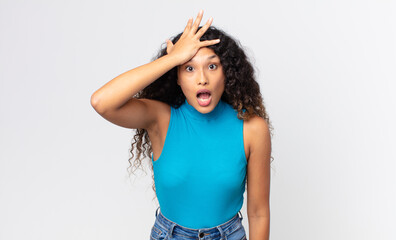 pretty hispanic woman raising palm to forehead thinking oops, after making a stupid mistake or...