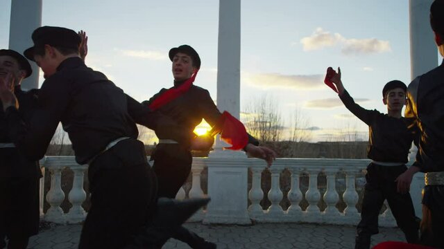 4K Group of Caucasian dancers in local black costumes perform traditional folk dance . Group of Men dancing traditional dance with handkerchief . Outdoor Shot on RED EPIC DRAGON Cinema Camera .