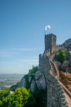 A wall of an ancient catle at the edge of the cliff with an old Portuguese flag - Moorish Castle, Sintra, Portugal - Vertical, 28.05.2021