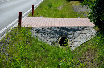 Sewer bridge through a ditch by the road. concrete hole with surroundings of stone paving. grassy...