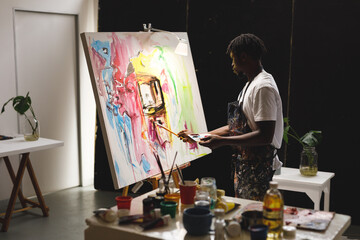 African american male painter at work painting on canvas in art studio - obrazy, fototapety, plakaty