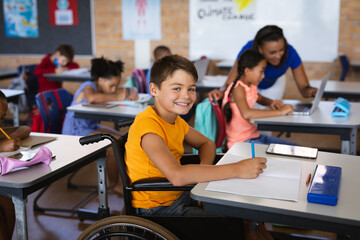 Portrait of disabled caucasian boy smiling while sitting on wheelchair in class at elementary school