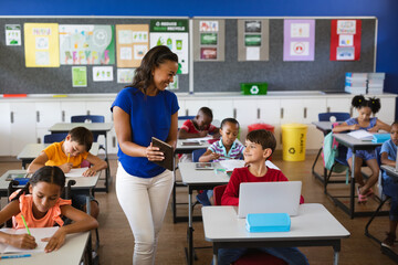 African american female teacher teaching caucasian boy to use digital tablet at elementary school