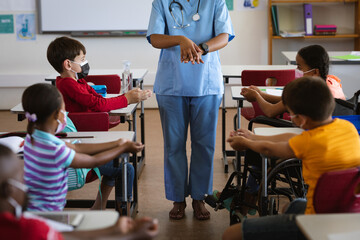 Obraz premium Mid section of female health worker showing students to use hands sanitizer at elementary school