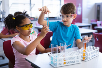 African american girl and caucasian boy holding test tube in science class at elementary school - Powered by Adobe