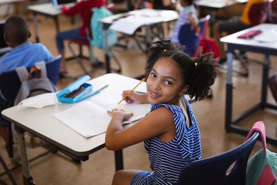 Portrait of african american girl smiling while sitting on her desk in class at elementary school