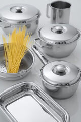 mesa com conjunto de panelas e escorredor de macarrão com espaguete cru
