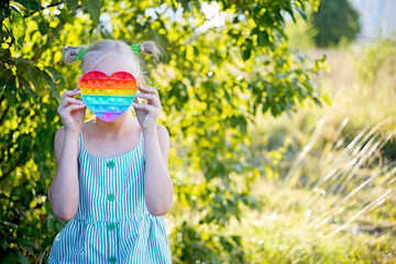 Blonde girl plays with colorful pop it. Funny trendy silicone antistress colorful sensory push toy popit and simple dimple. Flapping fidget. Rainbow color hart, helps with autism and stress reliever.