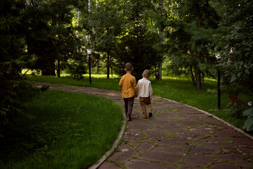 Fototapeta premium Two boys are walking along the alley. Two brothers are walking in the park