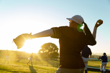 Diverse group of female baseball players warming up on field at sunrise, throwing and catching balls