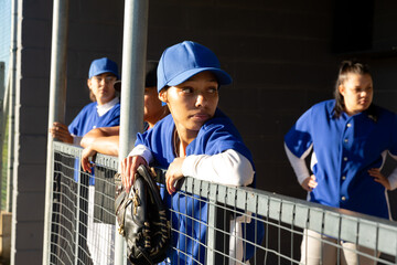 Diverse group of female baseball players standing in enclosure waiting before game