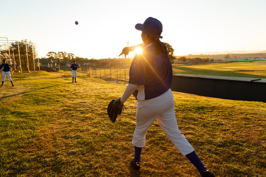 Diverse group of female baseball players warming up on field at sunrise, throwing and catching ball