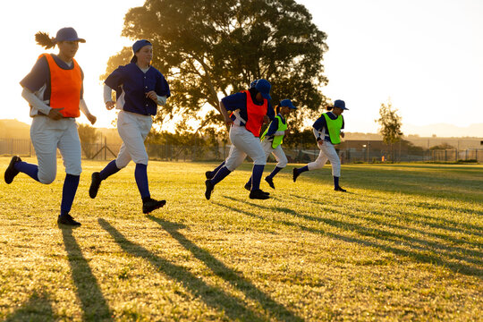 Diverse group of female baseball players warming up on field at sunrise, running - Powered by Adobe