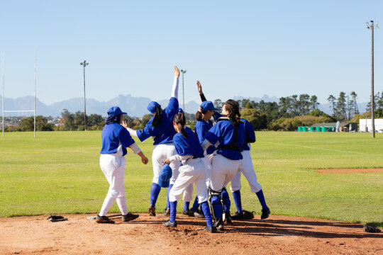 Diverse group of happy female baseball players celebrating on sunny baseball field after game - Powered by Adobe