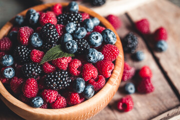 Ripe blackberries with leaves in a bowl on a wooden board on a dark background