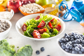 Healthy fresh salad with tomatoes olives and olive oil, surrounded by healthy food and exercise equipment