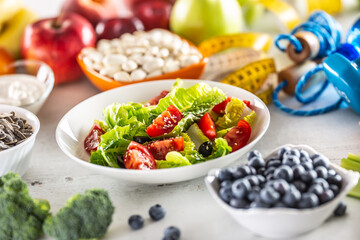 Healthy fresh salad with tomatoes olives and olive oil, surrounded by healthy food and exercise equipment