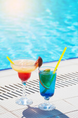 Two colorful cocktail glasses at the edge of swimming pool