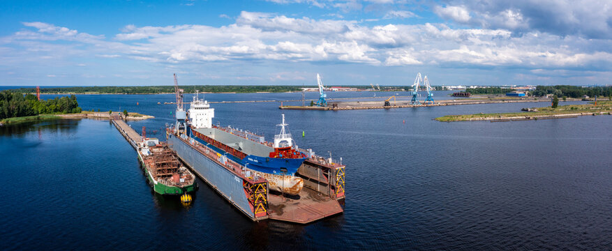 Riga, Latvia. June 10, 2021. Ship in floating dry dock under repair by sandblasting and painting in shipyard. Cargo ship at floating dry dock is being renovated