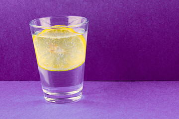 Mineral water with lemon in glass on purple background