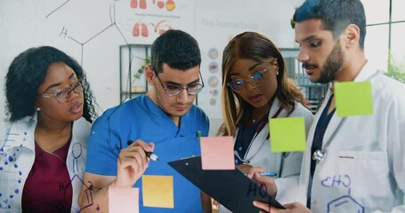 Science concept where attractive confident experienced mixed race group of chemists standing near glass board and writing structural formulas of chemical elements - Powered by Adobe