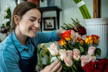 Young adult woman working in city street flower shop.She arranging flowers inside of shop.Small business concept.