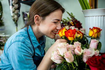 Young adult woman working in city street flower shop.She arranging flowers inside of shop.Small business concept.