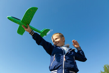 A six-year-old preschooler boy in a blue jacket launches a toy plane in nature against the...