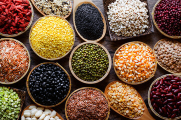 Collection of dry organic colorful cereal and grain seeds in wooden bowl in dark tone, consisted of bean, flax seed, goji berry, rice, peanut, job's tear, mung, and corn