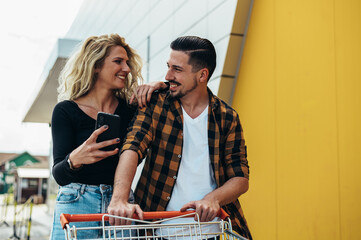 Young beautiful couple using smartphone while holding a shopping cart