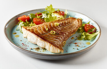 Appetizing fried fish fillet with mixed leaves and cherry tomatoes