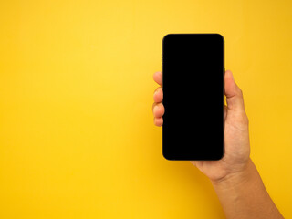 Fototapeta na wymiar Hand holding of a smartphone with a yellow background. Close-up photo. Space for text. Technology and communication concept