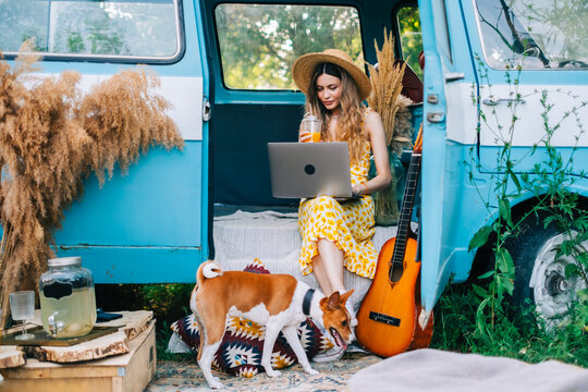 Young caucasian woman using laptop computer while sitting o a van outdoors.