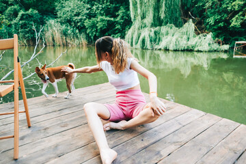 Young woman sitting on a wooden pier on a lake, and playing with her dog.