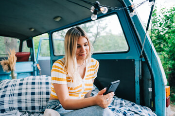 Portrait of young woman sitting in a van and using mobile phone, outdoors in nature. Enjoying...