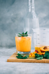 Ice lemonade in glass with peach pieces, fresh mint and ice cubes on the table.