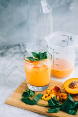 Ice lemonade in glass with peach pieces, fresh mint and ice cubes on the table.