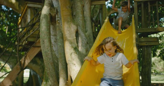 Young kids playing in treehouse going down the slide, summer lifestyle concept