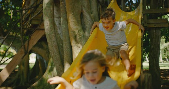 Young kids playing in treehouse going down the slide, summer lifestyle concept