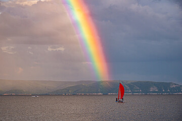 A bright rainbow over the river with a scarlet sail