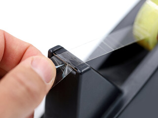 male hand is using a black dispenser of a transparent tape isolated on white background, close up