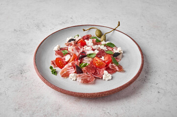Prosciutto coppa di parma ham slices with ricotta cheese, tomato, capers and basil on light plate,...