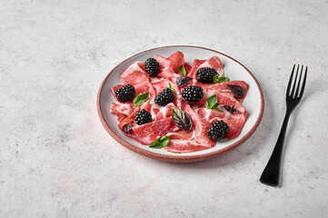 Close up slices of prosciutto ham coppa di parma with basil and blackberry on light plate and black fork with copy space - obrazy, fototapety, plakaty