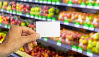 Empty plastic grocery card in hand on supermarket background. Grocery card for discounts and promotions in shops and supermarkets