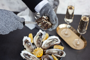 Hands of waiter in special gloves opening an oyster