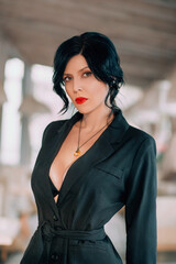 Obraz premium Closeup portrait of elegant modern middle age adult woman. Natural makeup, red lipstick. Deep neckline. Girl with black hair, beautiful dark black elegant classic jacket. Blurred building background