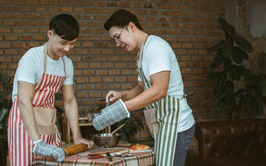 Portrait two handsome adult Asian men or friends wearing casual, aprons, holding cooking together in kitchen at home during holiday, smiling with happiness and confidence. LGBT, Hobby Concept.